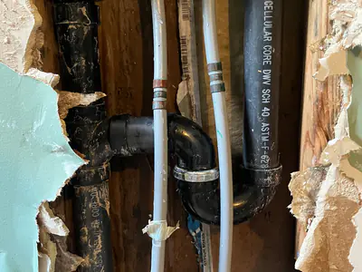 Water and drain pipes inside a wall opened up to repair the lines to a washing machine box in Carthage