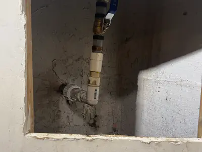 A new ball-valve shut-off on the main water line, reached through an access opening in the wall