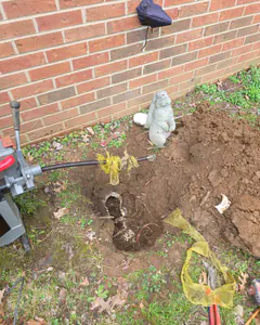 A cleanout dug out beside a brick wall with the sewer machine cable running into it, clearing a blocked main line in Old Hickory