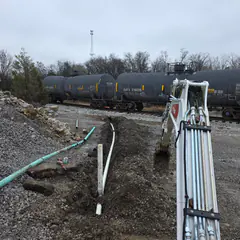 A commercial trench by a rail line with new pipe and a bundle of conduit.