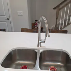 A double stainless kitchen sink with a new pull-down faucet in a kitchen island.