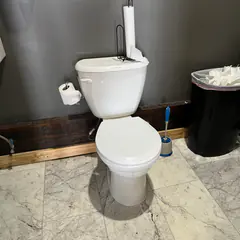 A toilet reset in a dark-walled restroom on marble-look tile.