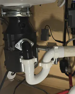 A garbage disposal with new white PVC drain piping under a sink.
