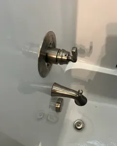 A brushed-nickel shower valve and tub spout on a white tub surround.