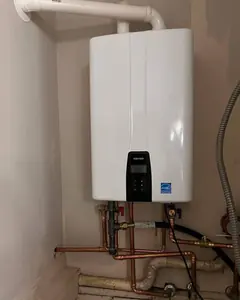 A white tankless water heater with its copper piping on a wall.
